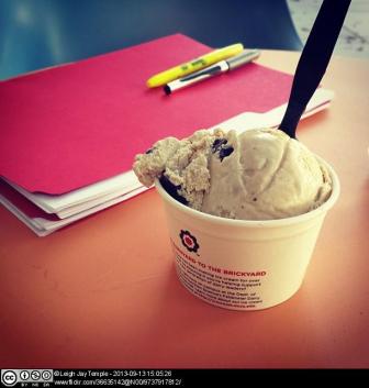 Ice cream tub with spoon on table beside folder and pens